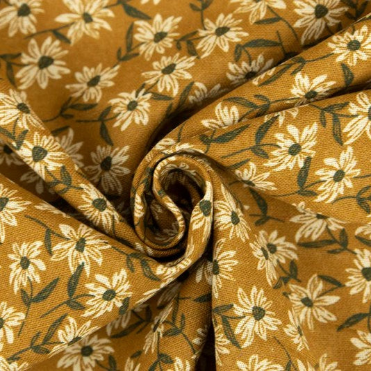 A close-up of draped fabric with a repeating floral print on a warm mustard-yellow background. The design features cream-colored daisy-like flowers with dark green centers and stems, arranged in a spiral fold.