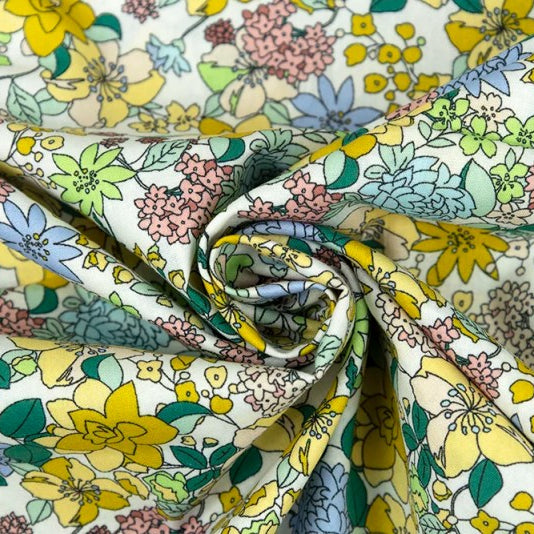 A close-up of a draped fabric with a dense floral pattern featuring yellow, pink, blue, and green flowers on a white background, arranged in a spiral drape.
