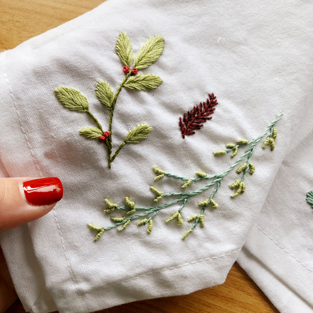 a hand holding Winter themed embroidered foliage 