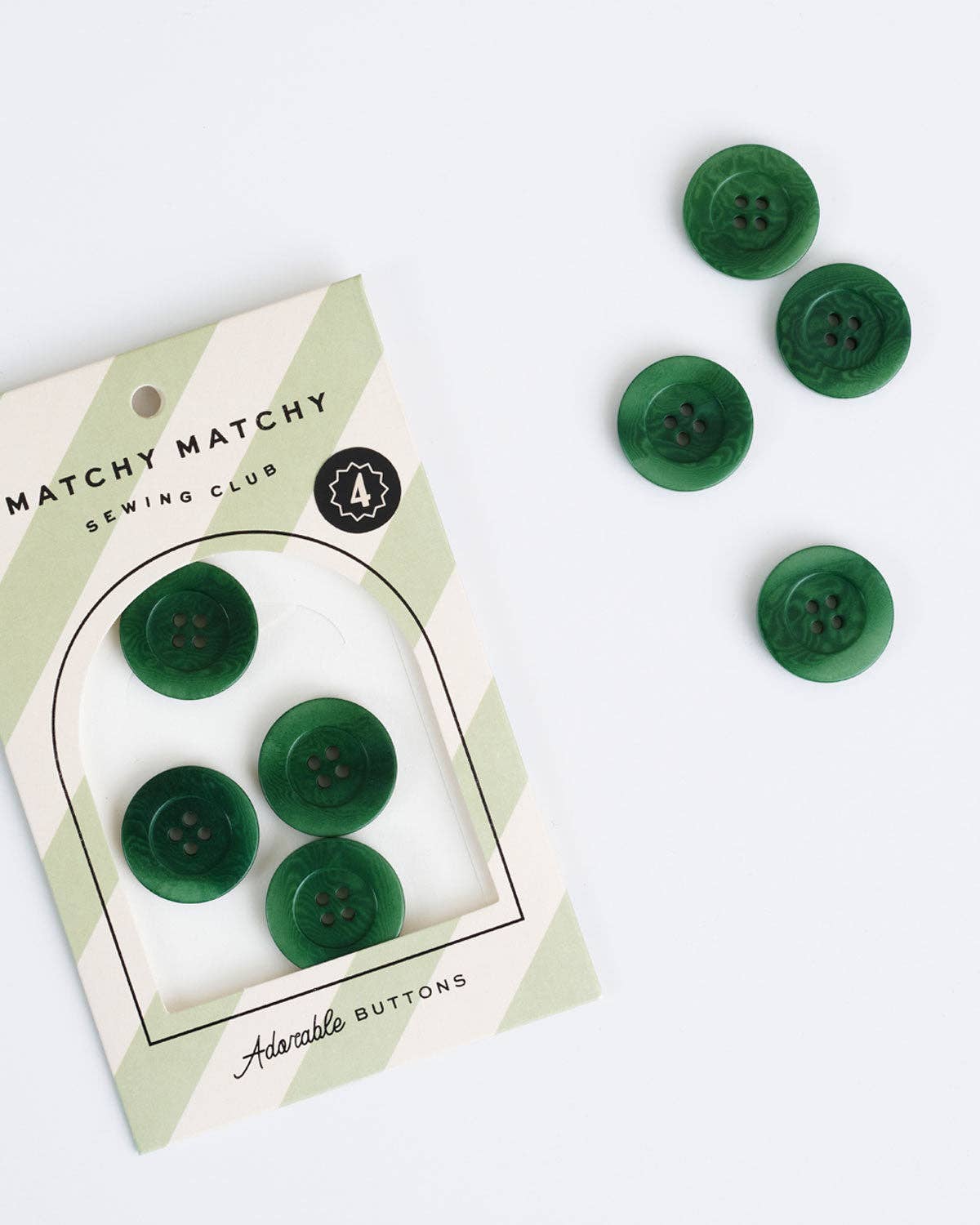 Set of 4 green  buttons wrapped in packaging with light green stripes on a white background.