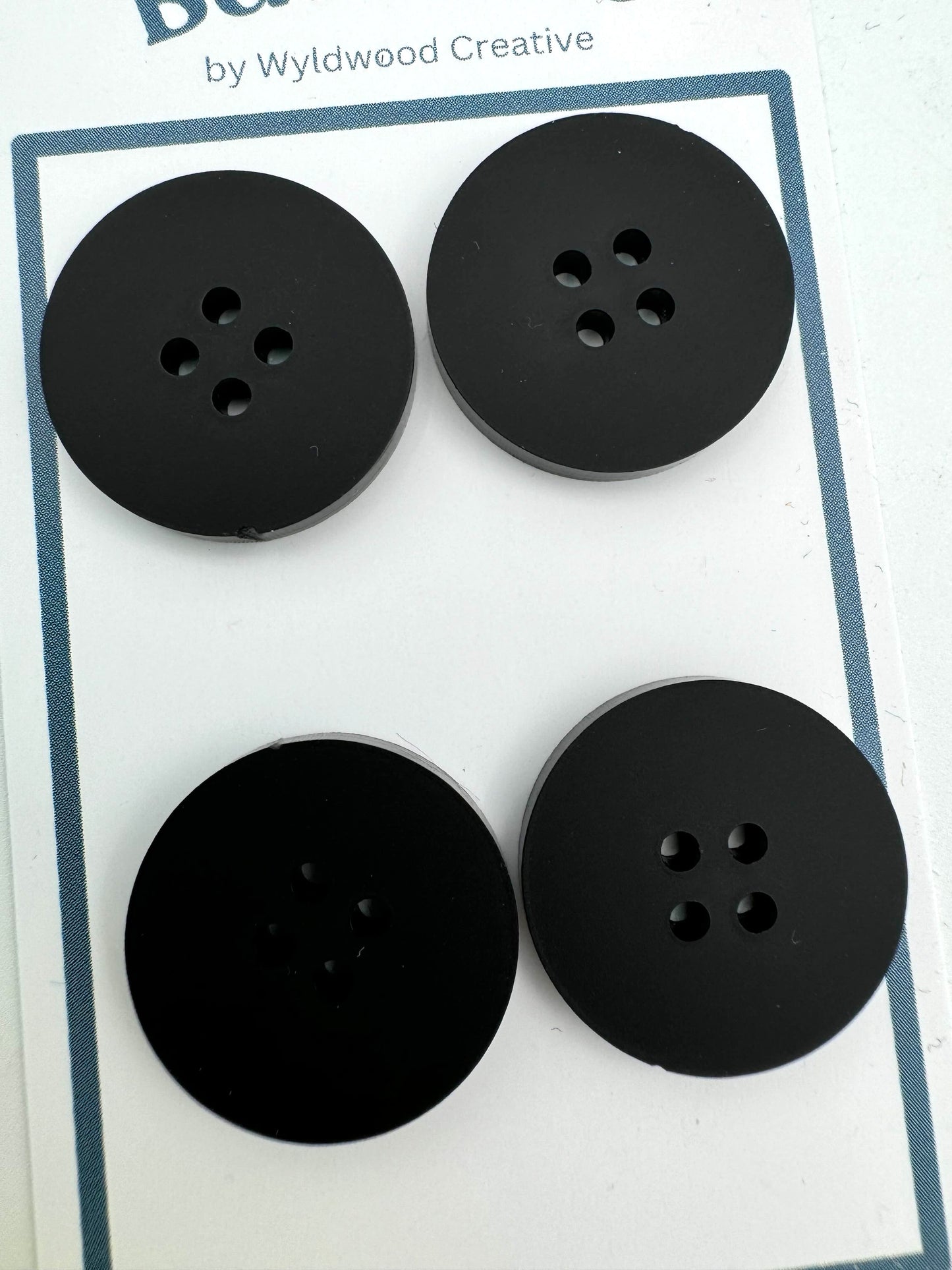 A close up of a set of 4 black buttons on a paper card