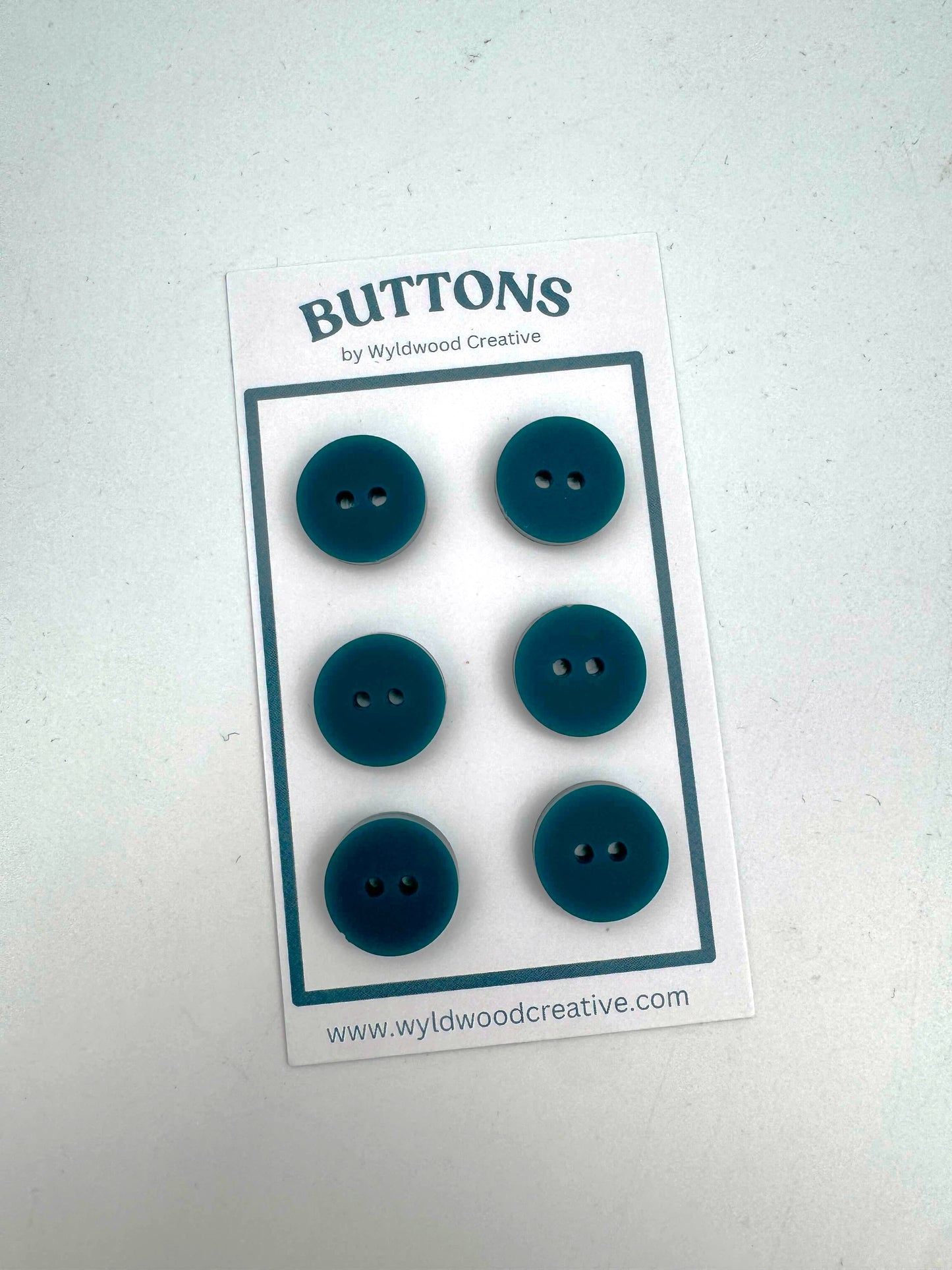 A set of 6 teal buttons on a paper card against a white background