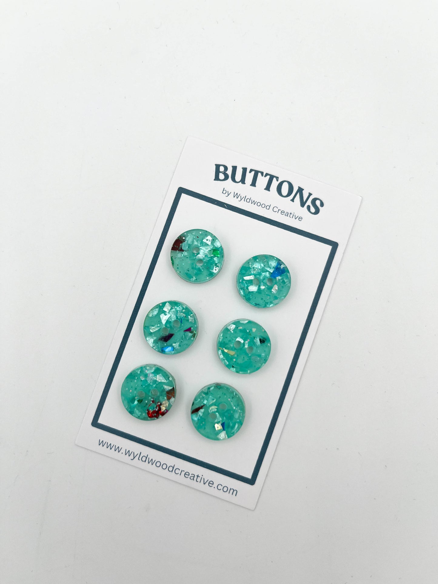 A set of 6 turquoise glitter buttons on a paper card against a white background