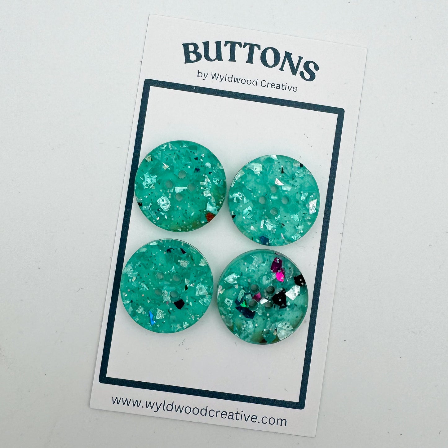a set of 4 turquoise glitter buttons on a paper card against a white background