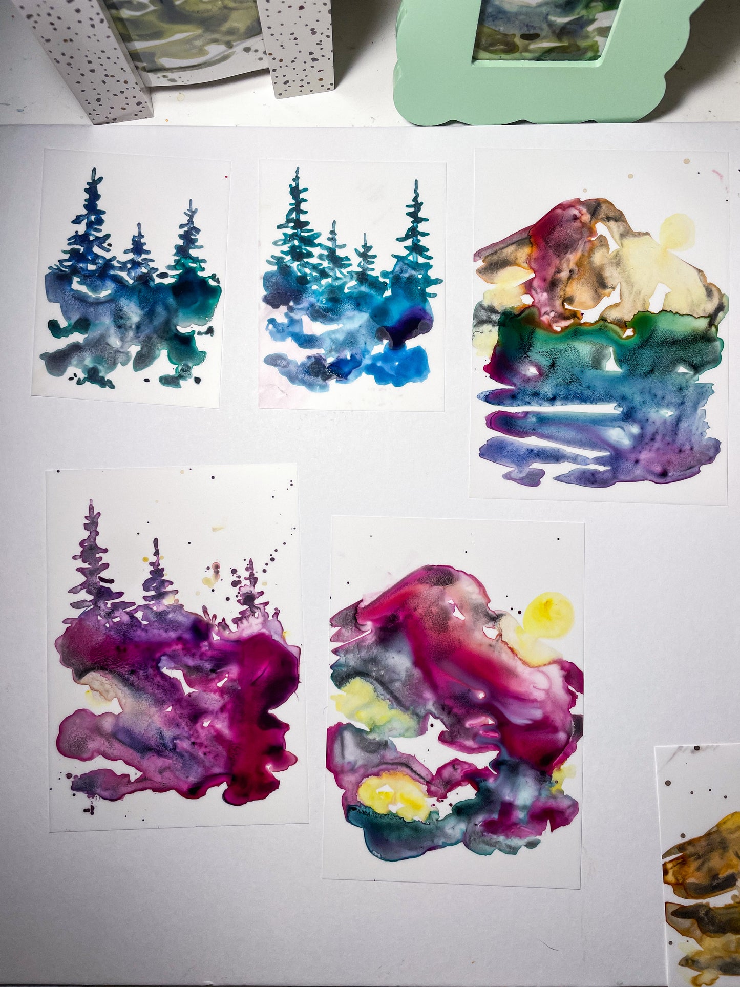 Five abstract watercolor landscape paintings - two with trees in greens and blues, one with trees in reds and purples, and two with Mount Rainier multicolors - painted in a watercoloring class at Wyldwood Creative in Renton