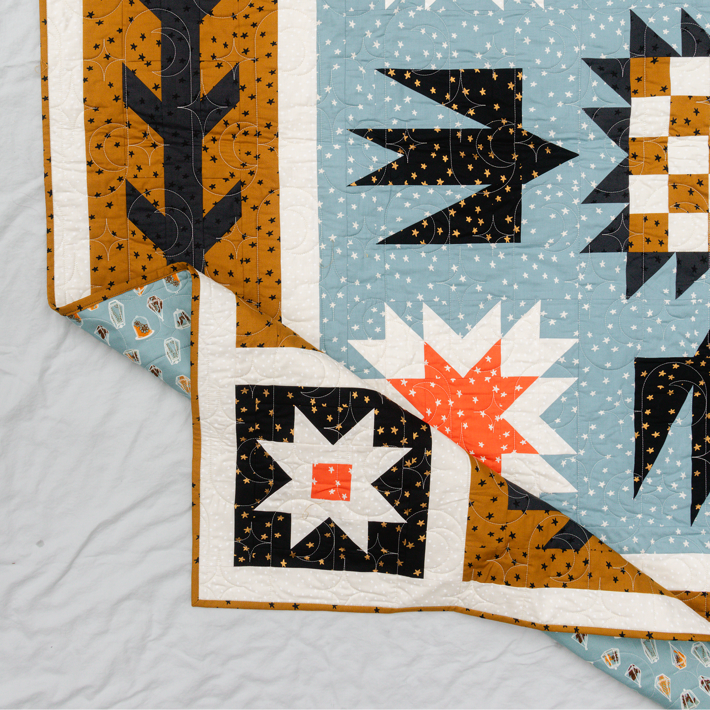 geometric quilt pattern featuring birds and stars, corner edge of quilt folded over