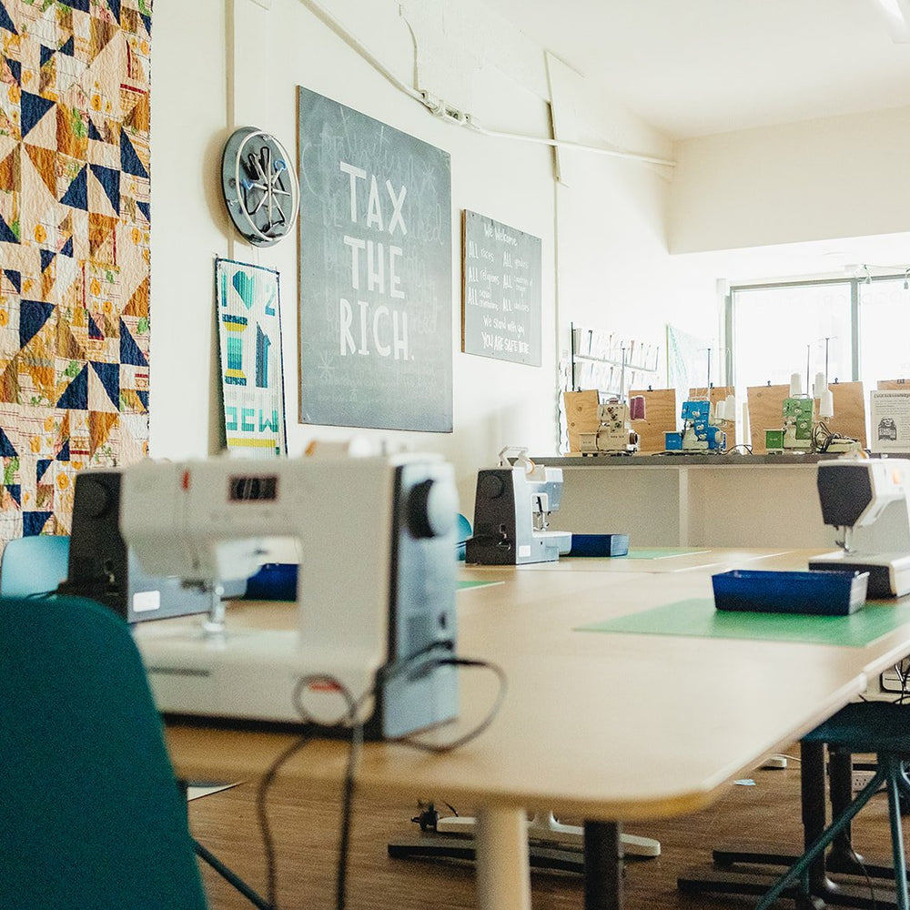 Side angle photograph of the class learning space with sewing machines, sergers, and other tools at Wyldwood Creative in Renton.