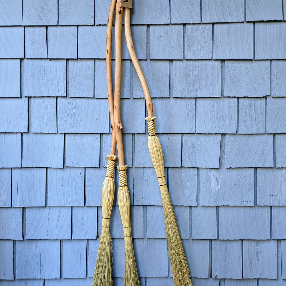 Three cobwebbers (long skinny hand brooms) hanging from a hook on an outdoor wall made in a crafting class at Wyldwood Creative Renton.