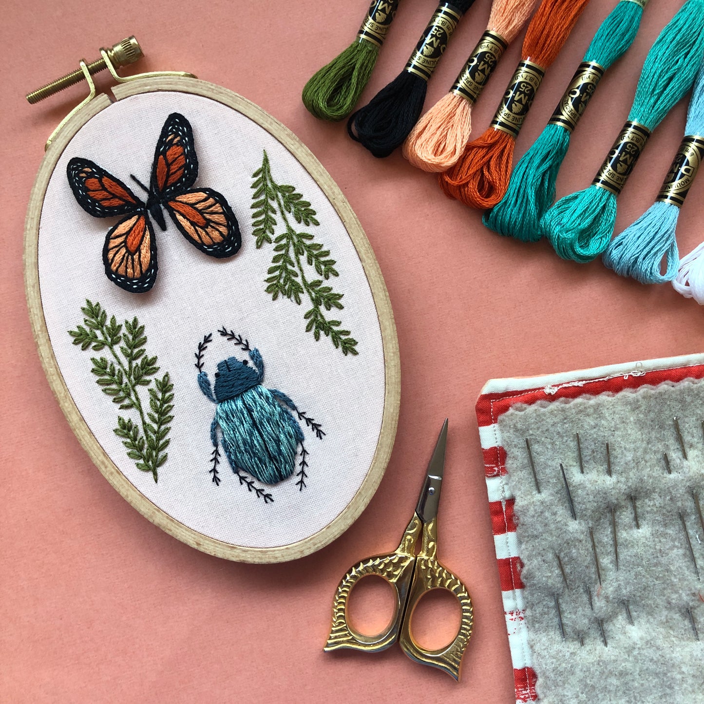 Embroidered monarch Butterly pin in 3D sitting on another embroidery with greenery and a blue beetle - made in a class at Wyldwood Creative in Renton