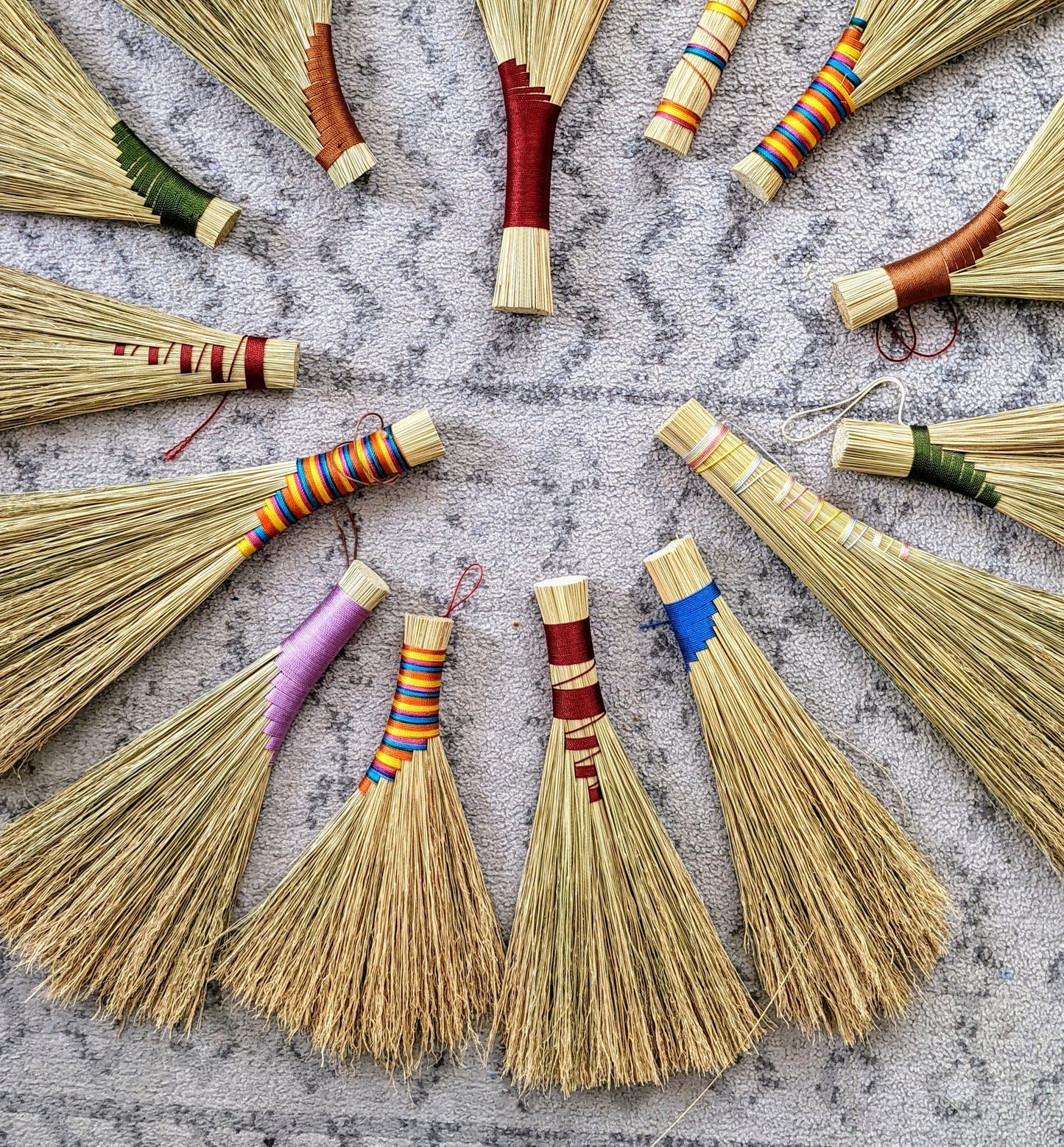 A circle display of straw hand brooms on a carpet, made at a crafting class at Wyldwood Creative Renton