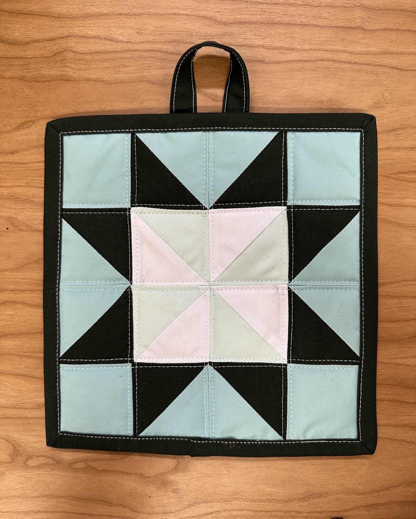 Quilted pot holder with geometric pattern on a wooden surface