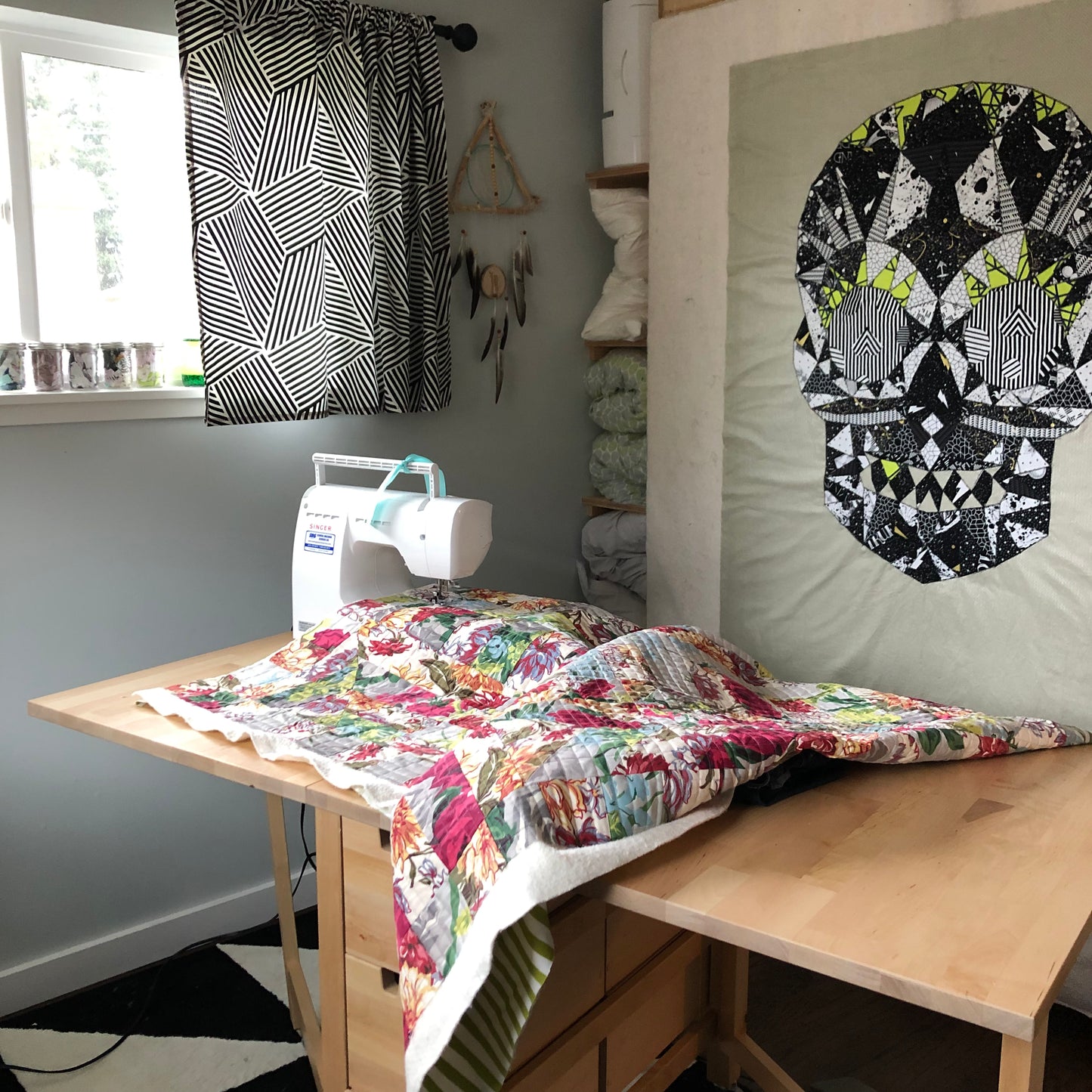 Sewing machine with quilt on a table in a room at home next to a winder and a skull quilt hanging on the wall - taken during at virtual Intro to Quilting class from Wyldwood Creative
